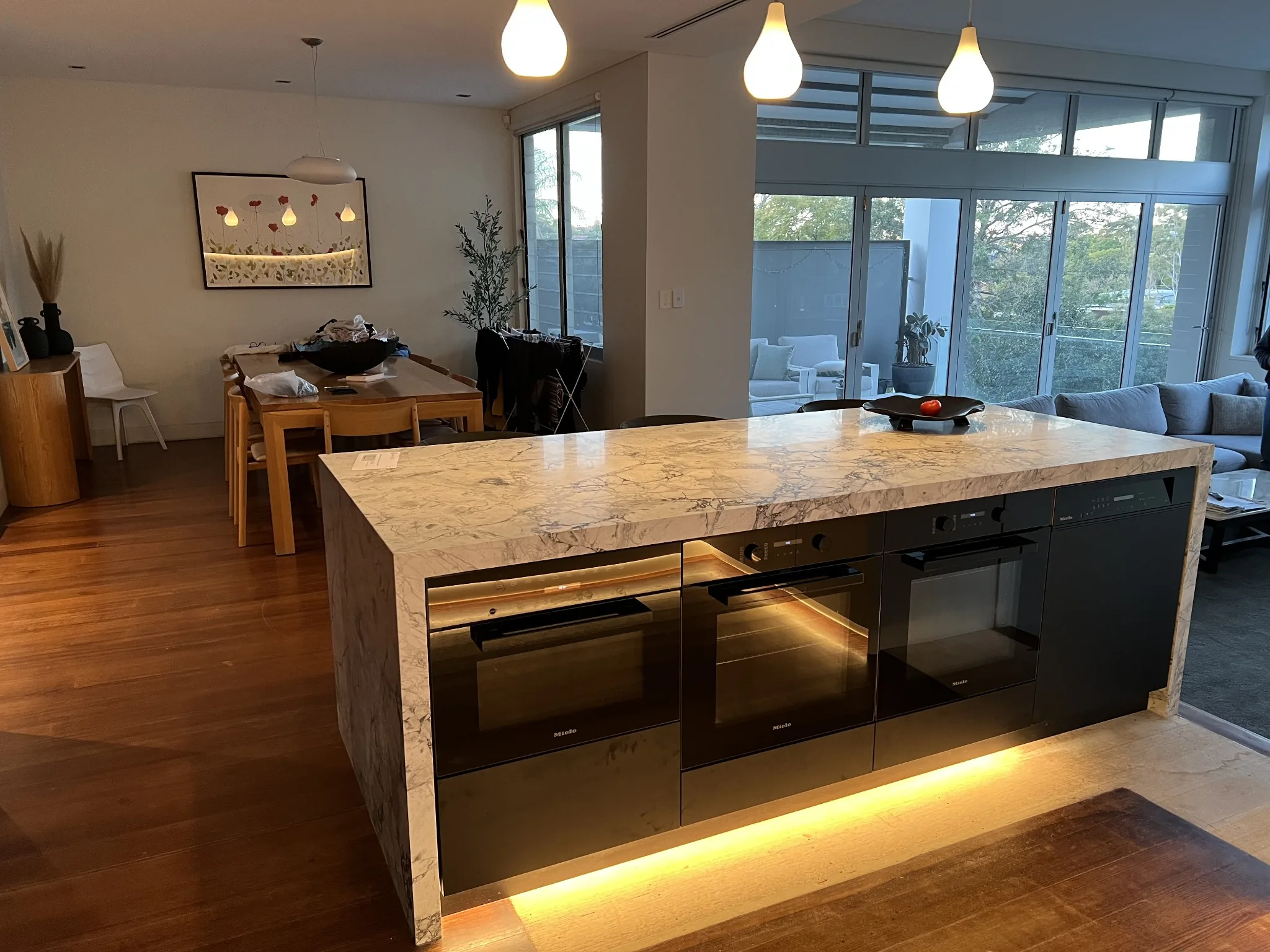 Stone waterfall island with integrated ovens and warm lighting